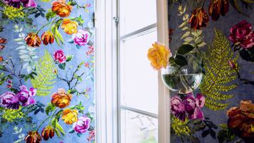 A room with floral wallpaper, a window, and a vase with flowers.