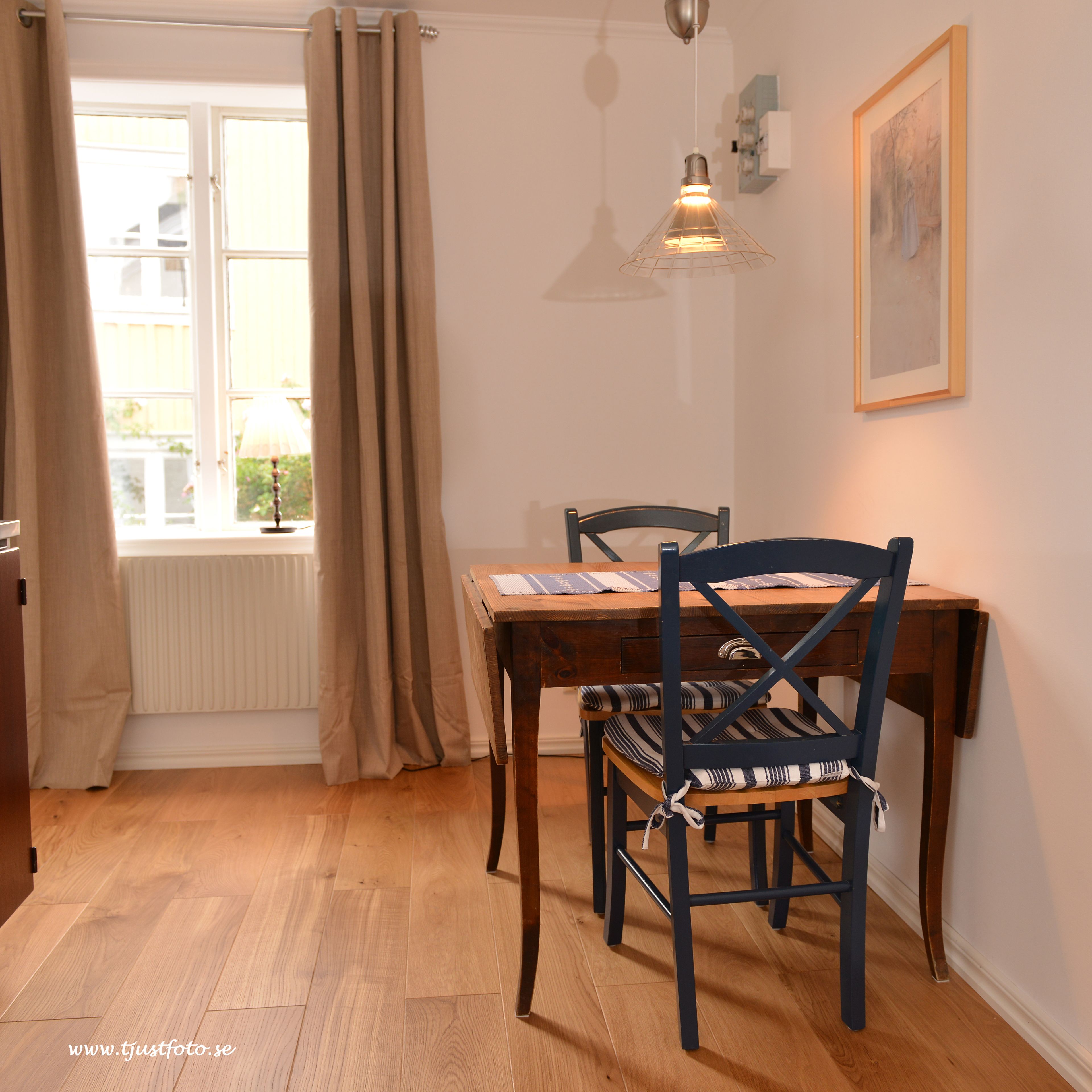 A dining area with a wooden table and chairs, a window with curtains, and a hanging light fixture.
