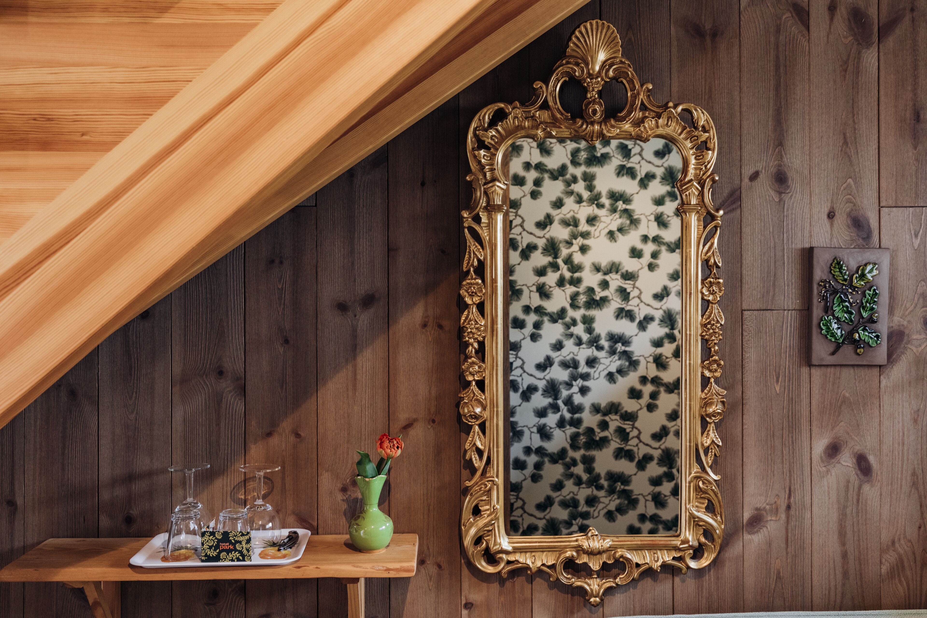 A wooden wall with a decorative mirror and a small table with a vase and glasses.