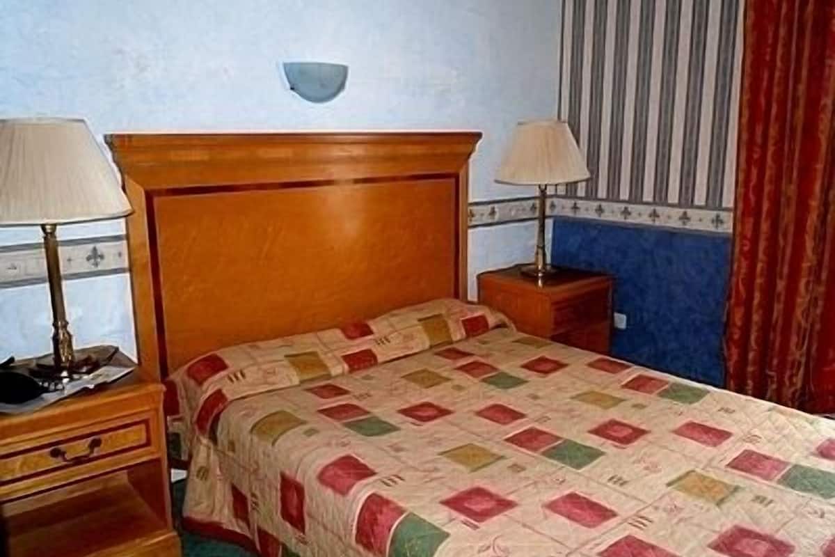 A single bed with a wooden headboard, two bedside tables with lamps, and a wall-mounted light fixture.