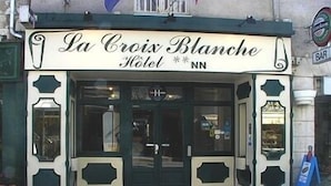 The facade of La Croix Blanche Hotel with a classic architectural style, featuring a prominent entrance and a visible bar sign.