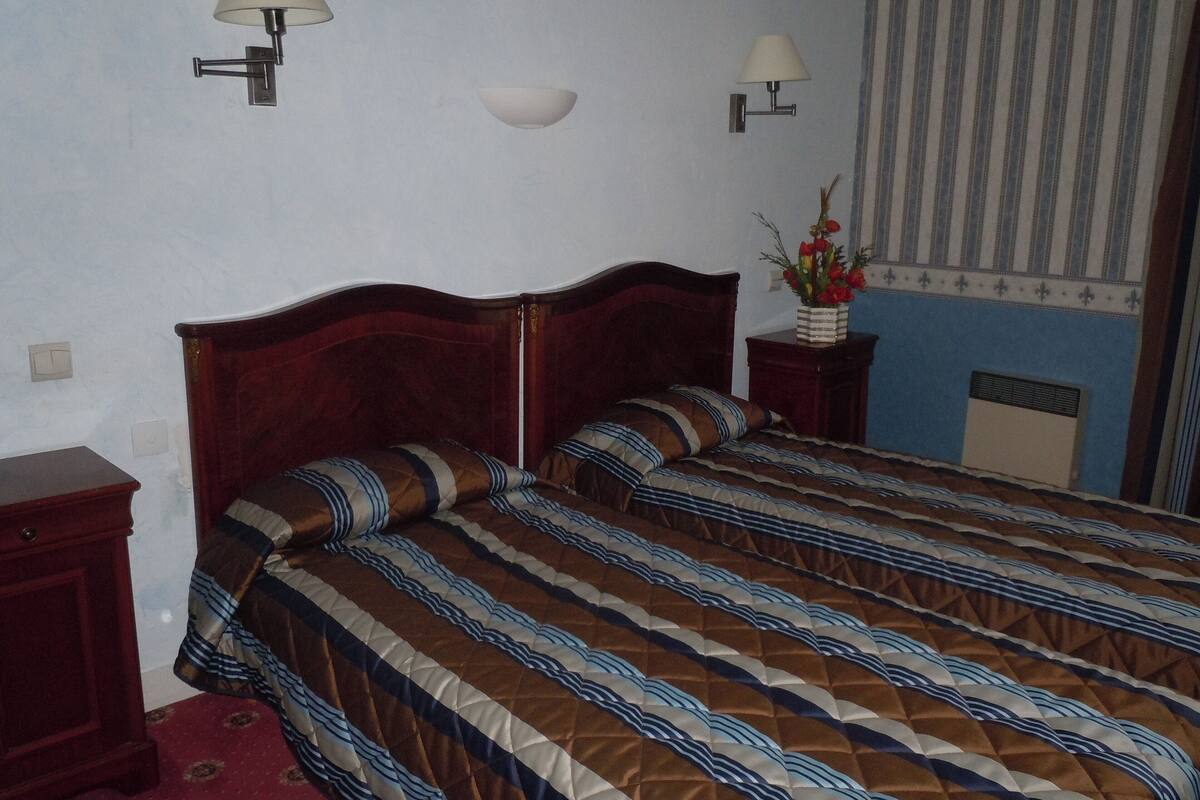A bedroom with a wooden bed, striped bedding, two bedside tables, wall-mounted lamps, and a window with striped curtains.