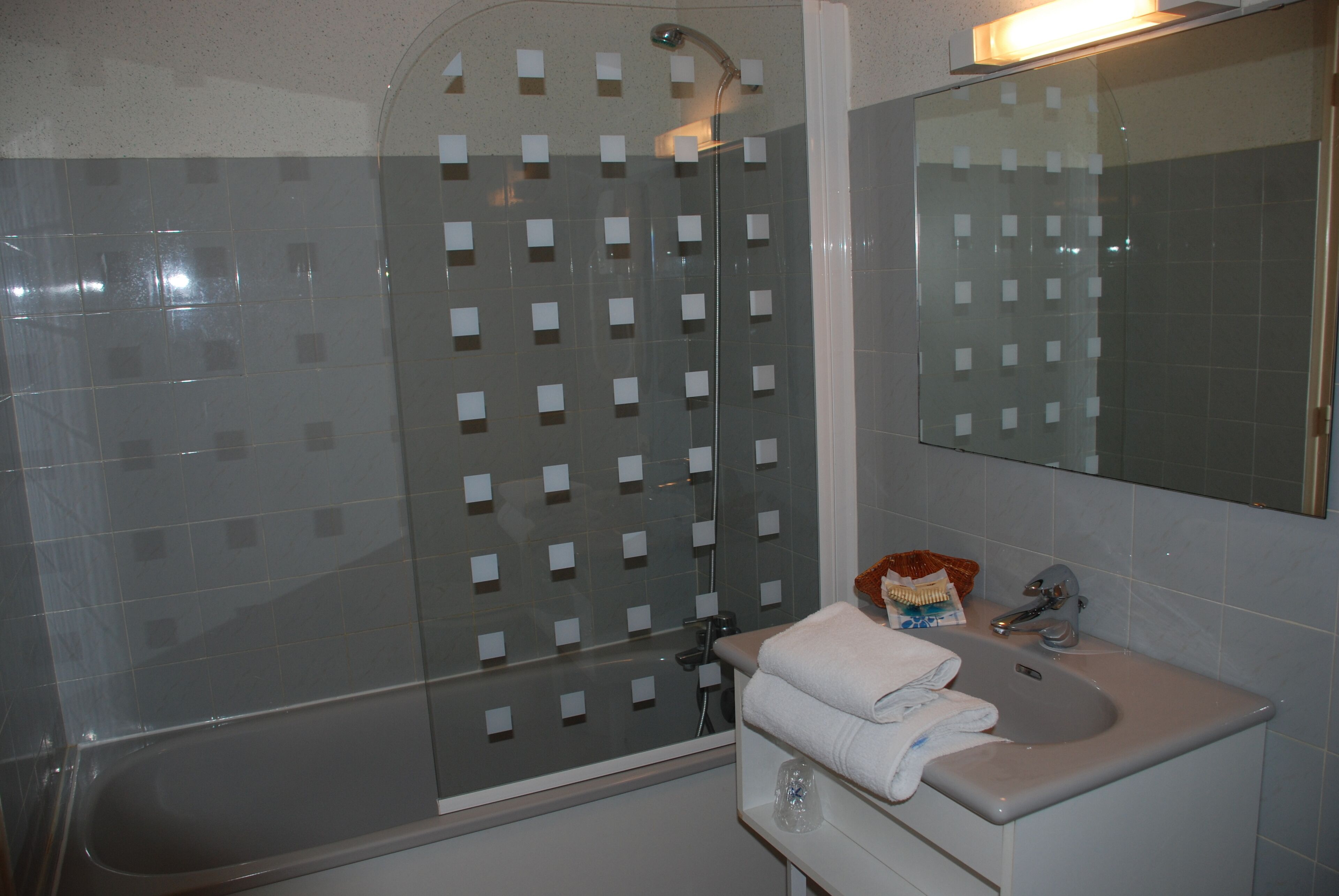 Un baño con cabina de ducha de vidrio, lavamanos con espejo y un perchero para toallas.