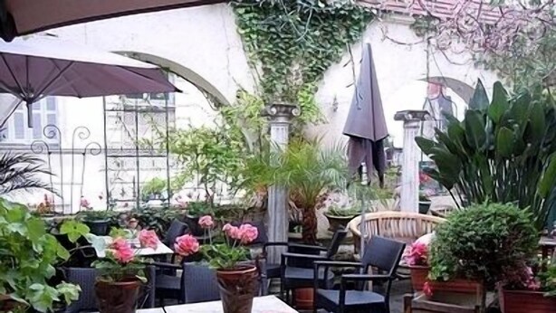An outdoor patio with tables and chairs, surrounded by potted plants and a pergola.
