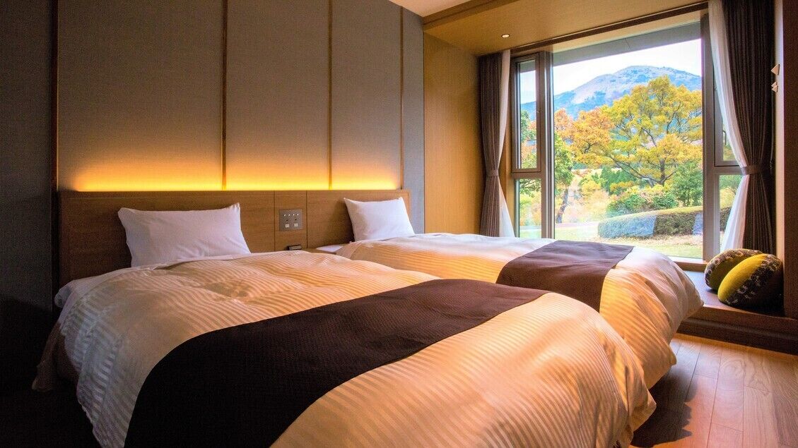 Habitación de hotel con dos camas, un ventanal con vistas a árboles y montañas, y suelo de madera.