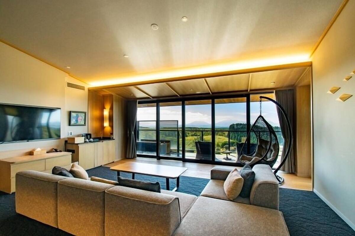 A modern living room with a large TV, a sofa, a coffee table, and a view of the outdoors.