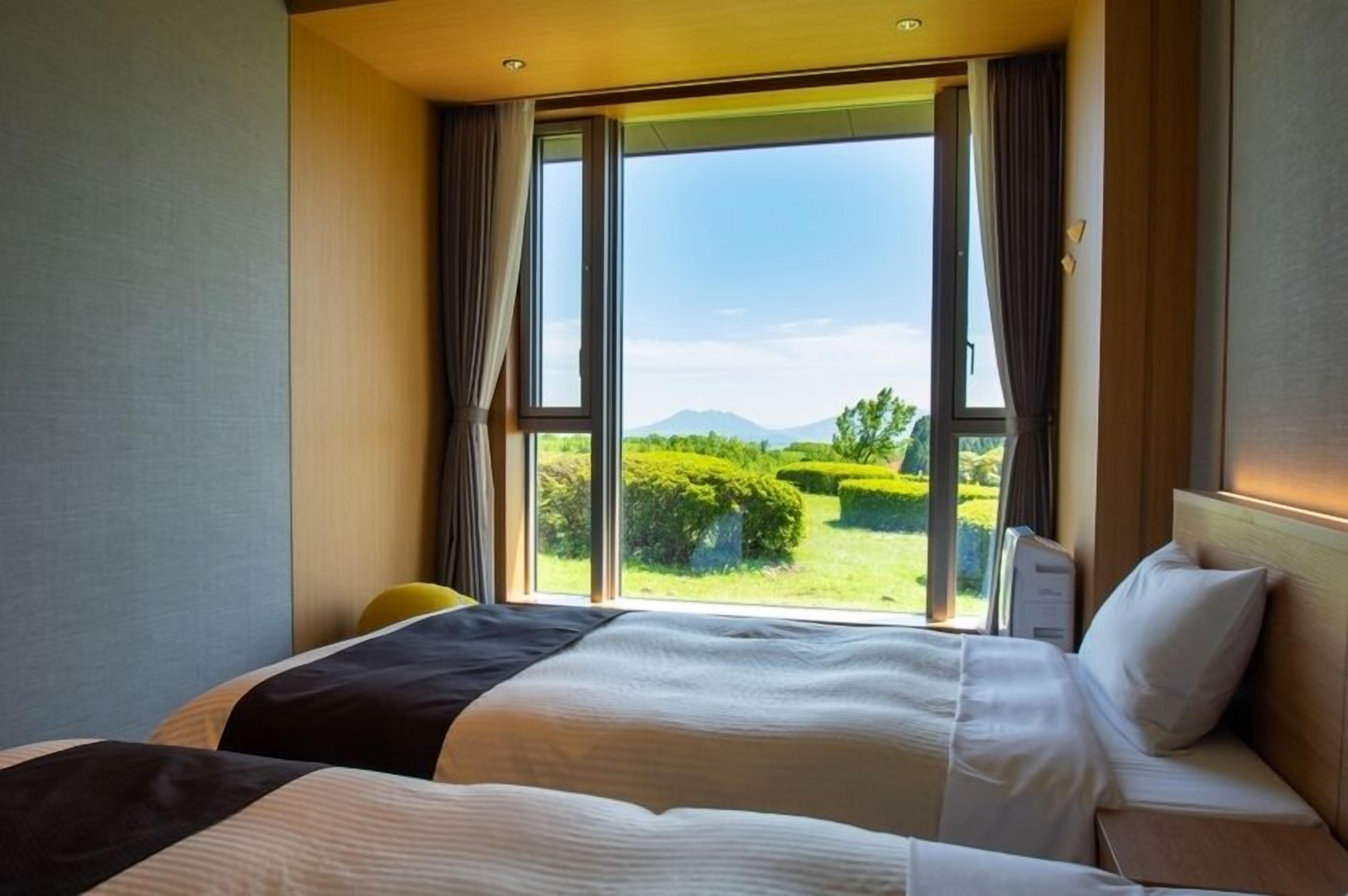 Habitación de hotel con una cama grande, un escritorio y vistas a un jardín cuidado y montañas.