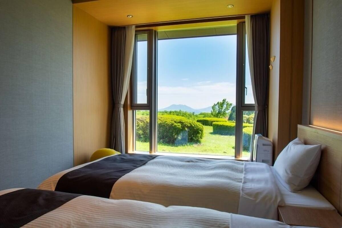 A hotel room with a large bed, a desk, and a view of a well-manicured garden and mountains.