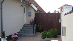 A residential property with a white exterior, a brown wooden gate, a small garden with potted plants, and a brick pathway leading to the entrance. - Amalie B&B Apartments (Odense)