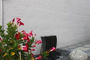 A white brick wall, a black planter with pink flowers, and a stone structure. - Amalie B&B Apartments (Odense)