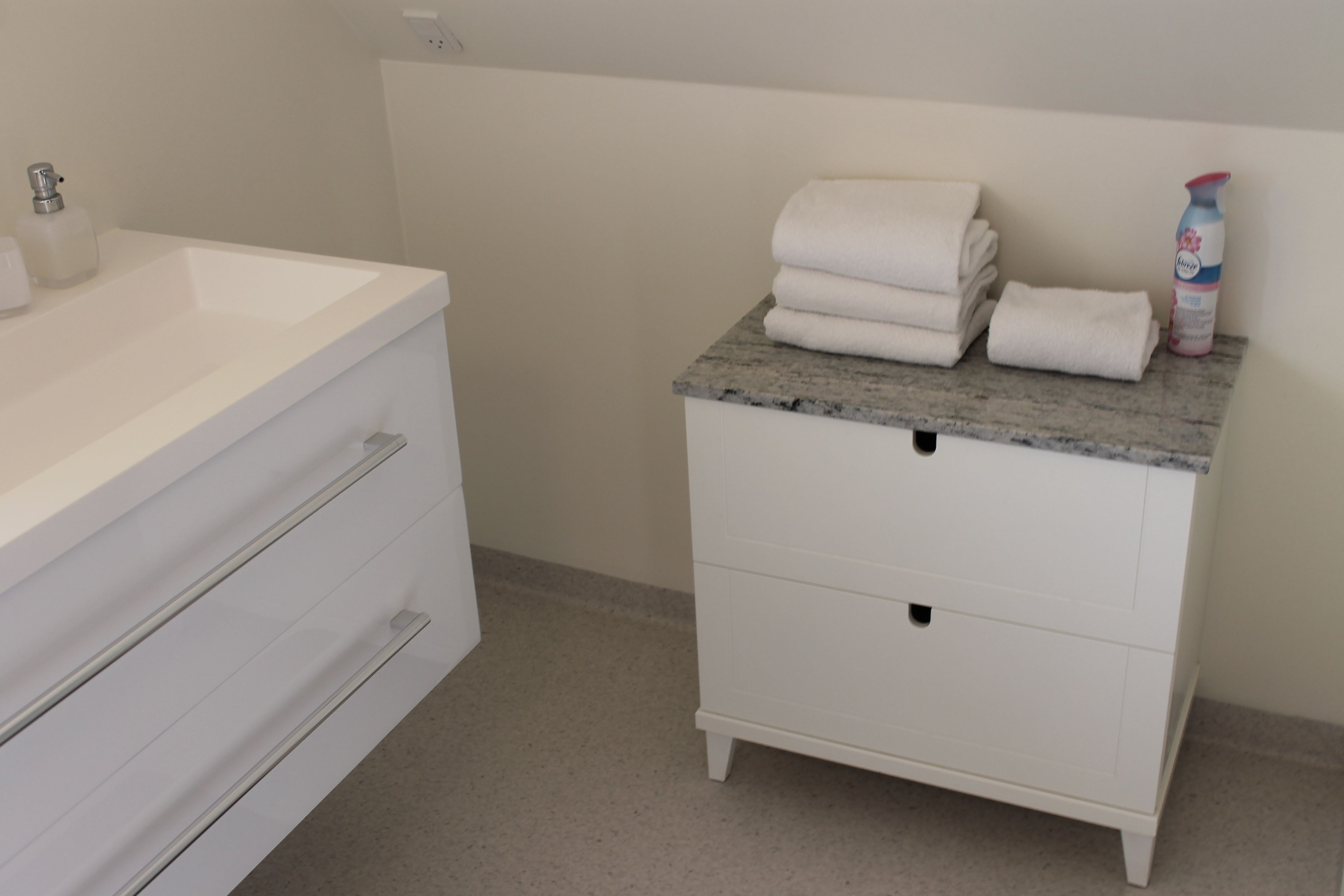 Un baño con lavamanos blanco, tocador con encimera de mármol y una botella de jabón para manos.