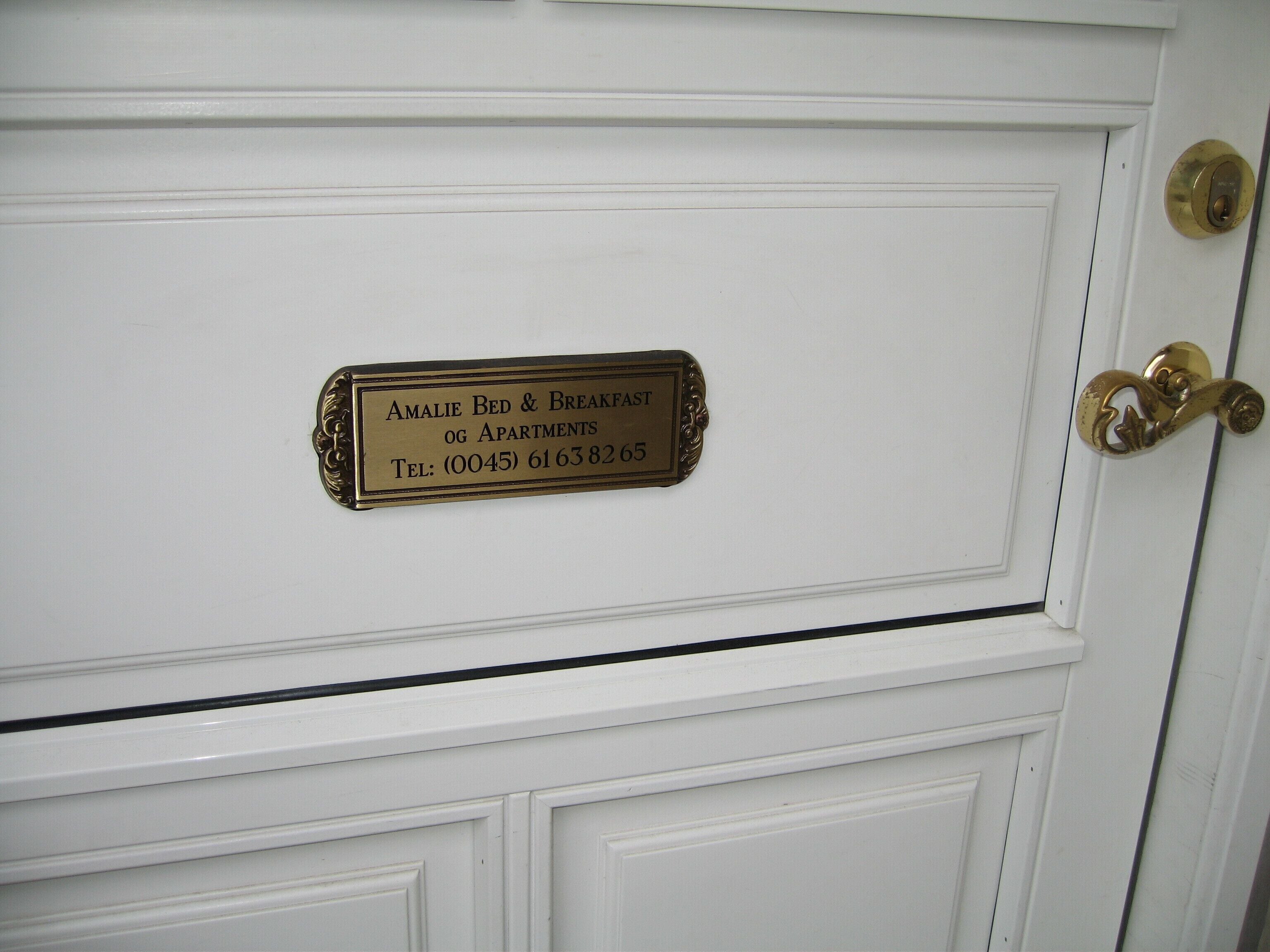 Una puerta blanca con una placa de latón que dice "Amalie Bed & Breakfast" y un número de teléfono.