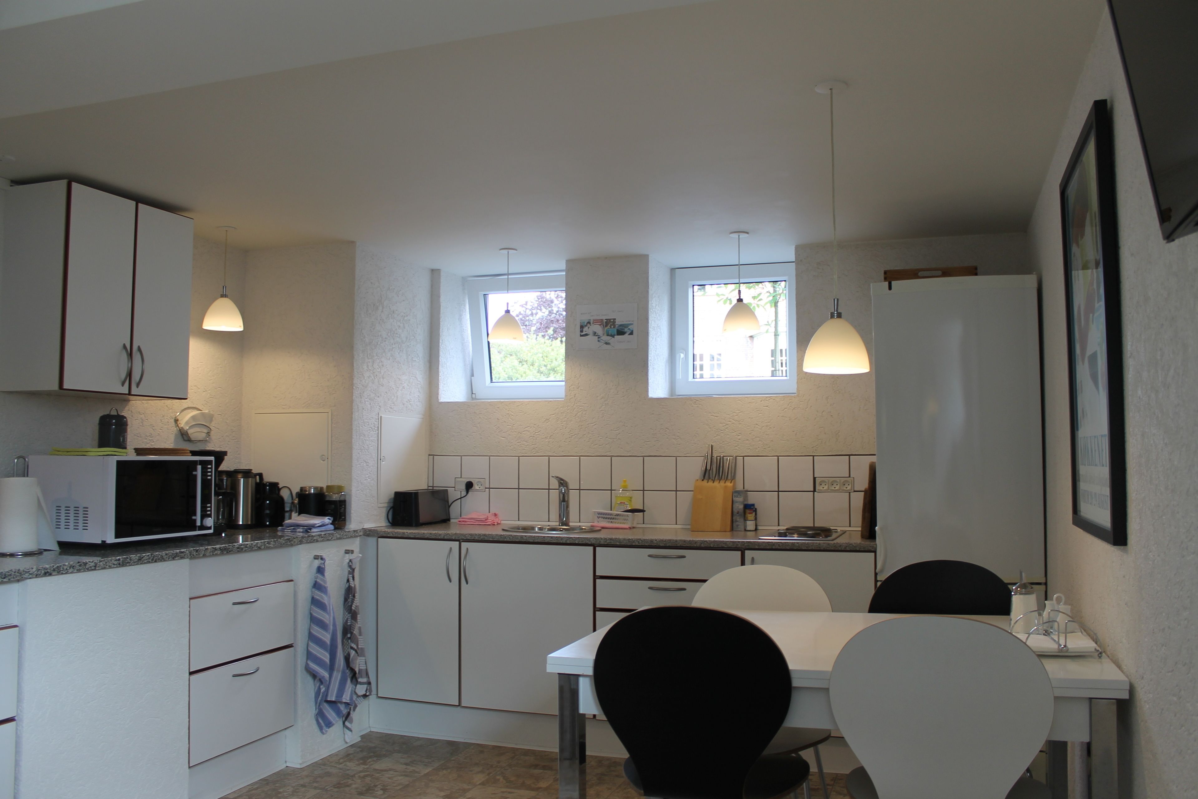 A modern kitchen with white cabinets, a dining table with chairs, and pendant lights.