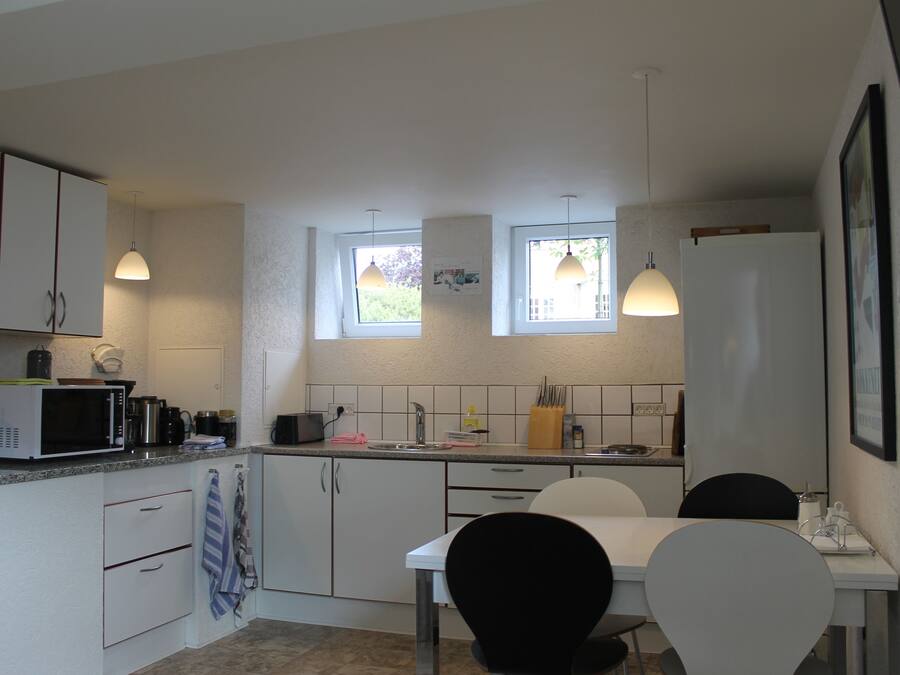 A modern kitchen with white cabinets, a dining table with chairs, and pendant lights.