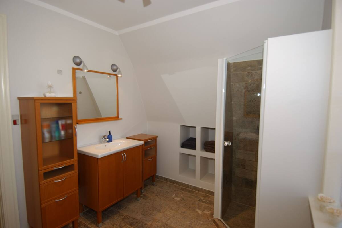 A bathroom with a wooden vanity, a mirror, a sink, and a shower area.
