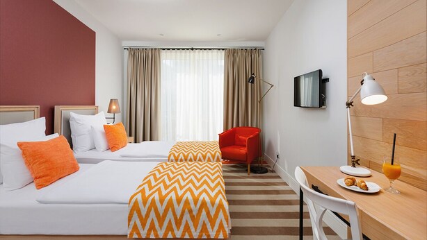 A hotel room with two beds, a desk, a chair, a TV, and a window with curtains. - Amalie B&B Apartments (Odense)