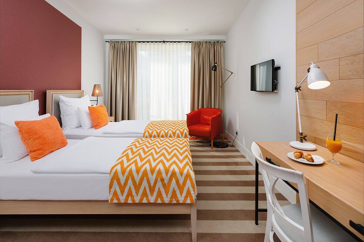 A hotel room with two beds, a desk, a chair, a TV, and a window with curtains.