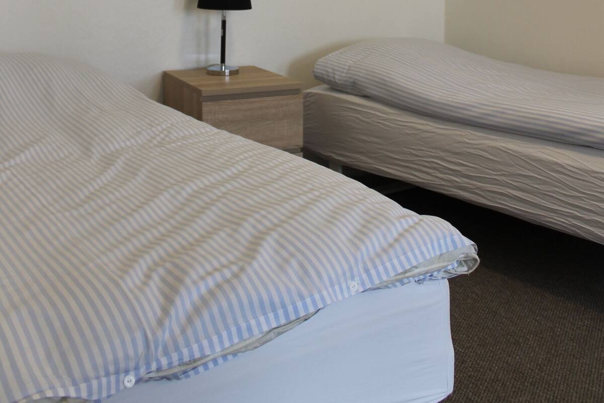 A hotel room with two beds, a nightstand with a lamp, and two framed pictures on the wall.