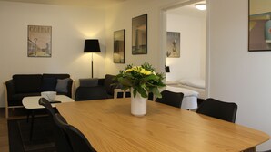 A modern room with a wooden dining table, black chairs, a white vase with flowers, a black lamp, and artwork on the walls. - Amalie B&B Apartments (Odense)