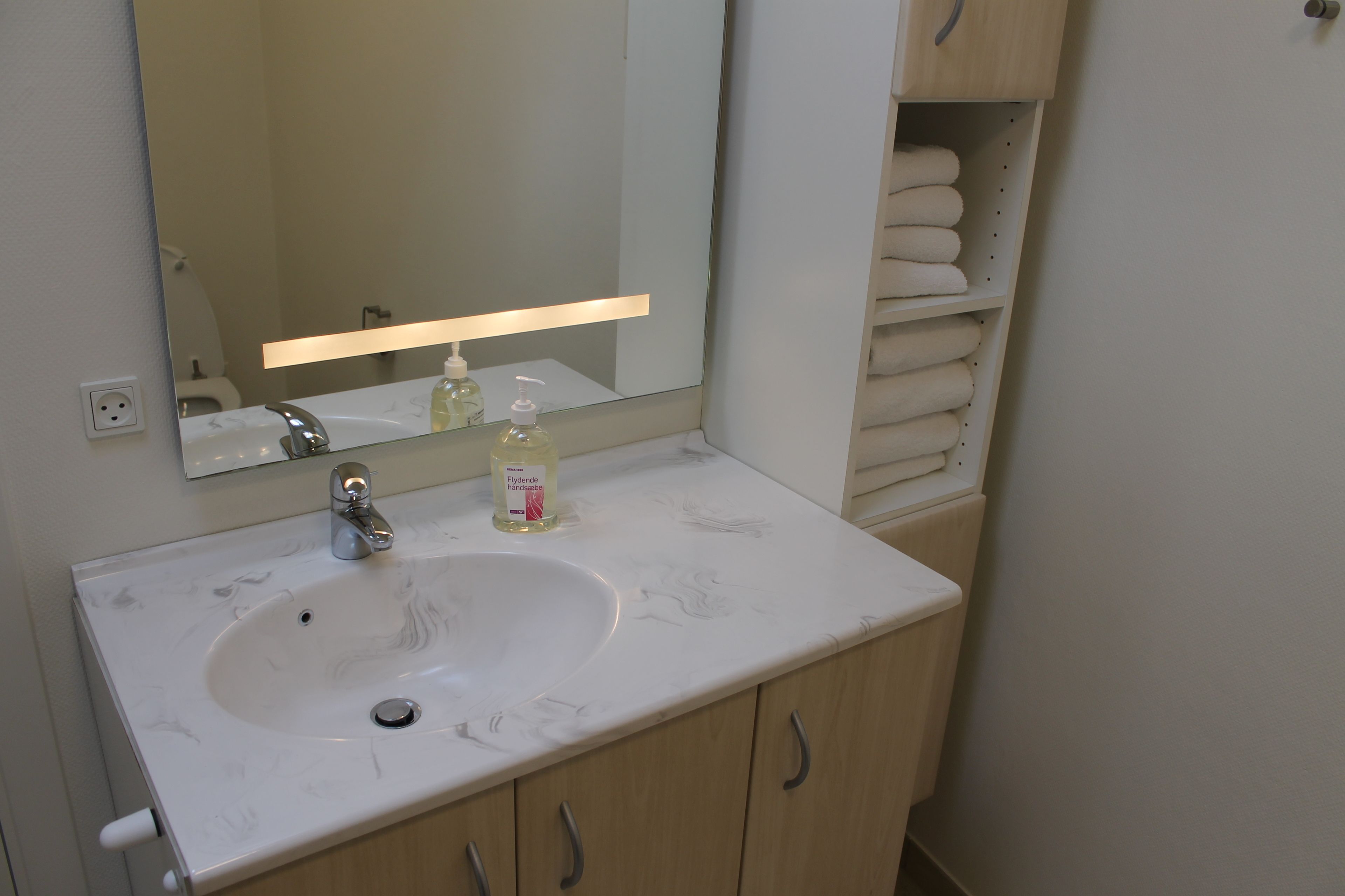 Un baño con un lavabo blanco, un espejo, un dispensador de jabón y un perchero para toallas.