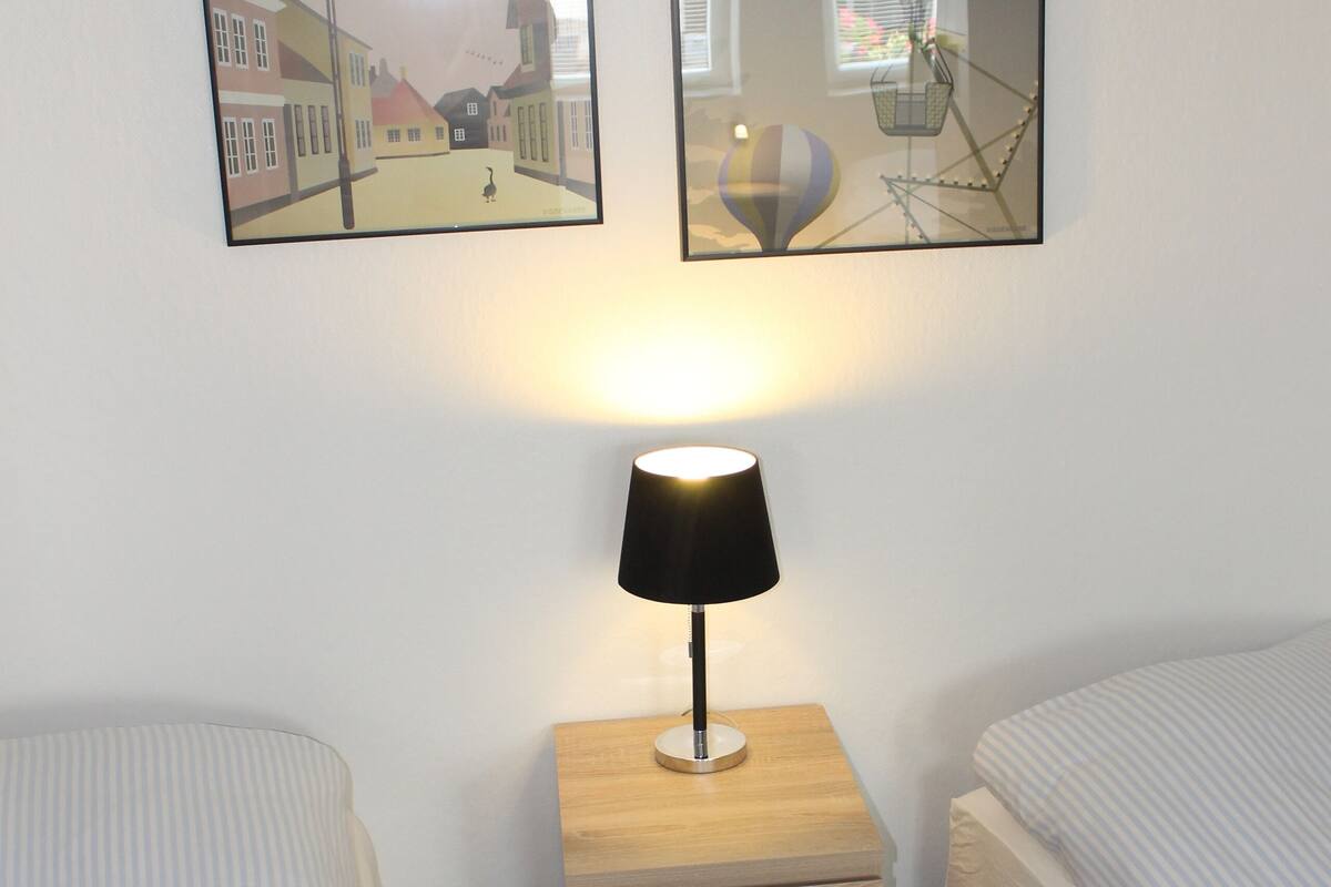 A hotel room with two beds, a nightstand with a lamp, and two framed pictures on the wall.