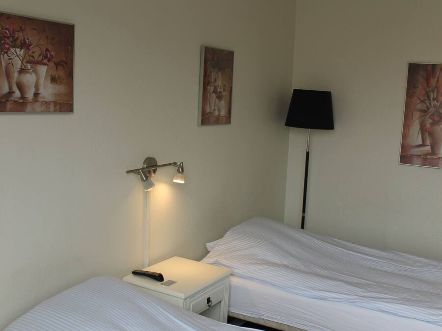 Habitación de hotel con dos camas, una mesita de noche con lámpara y obras de arte en la pared.