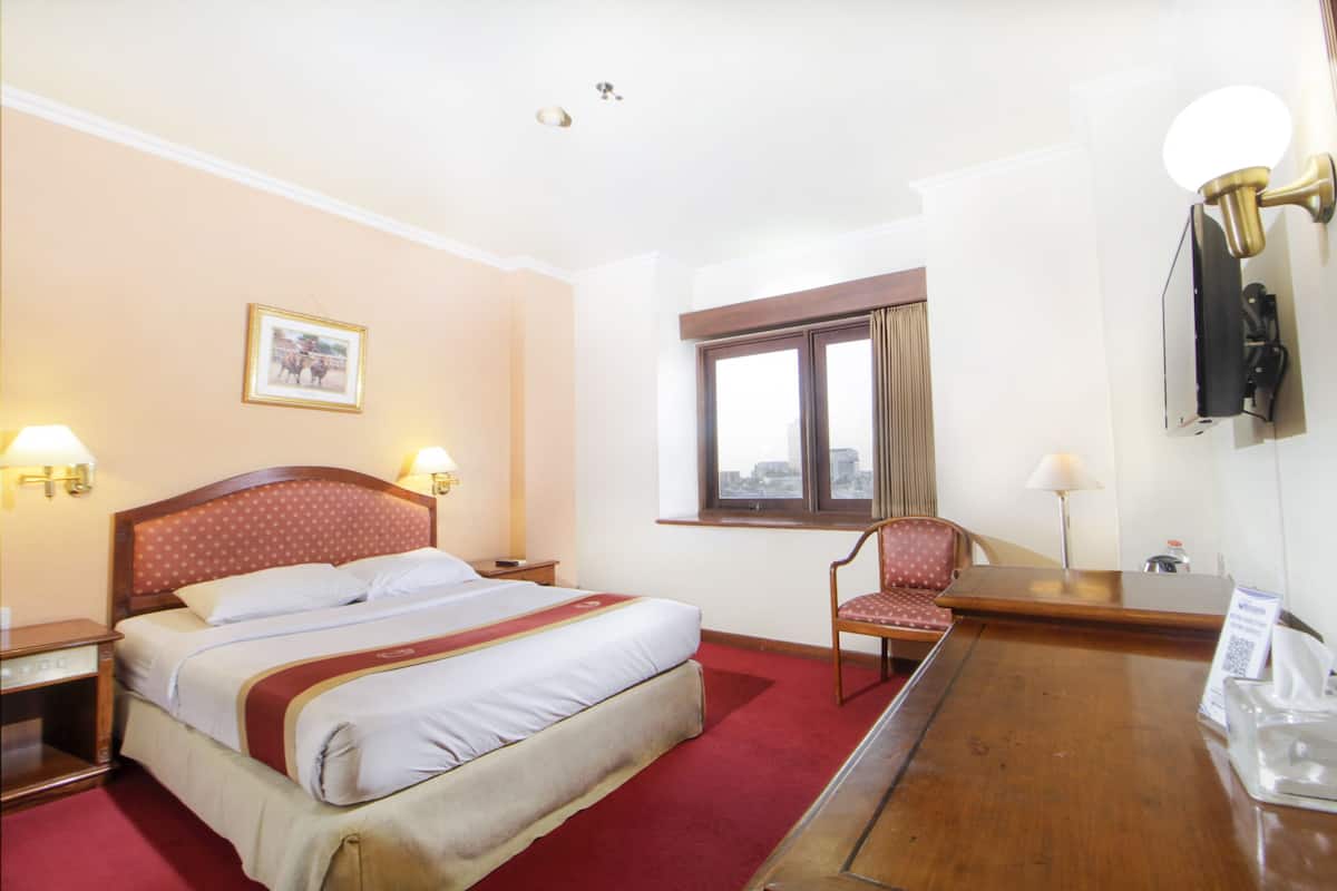 Ein Hotelzimmer mit einem großen Bett, einem Sessel, einem Schreibtisch und einem Fenster.