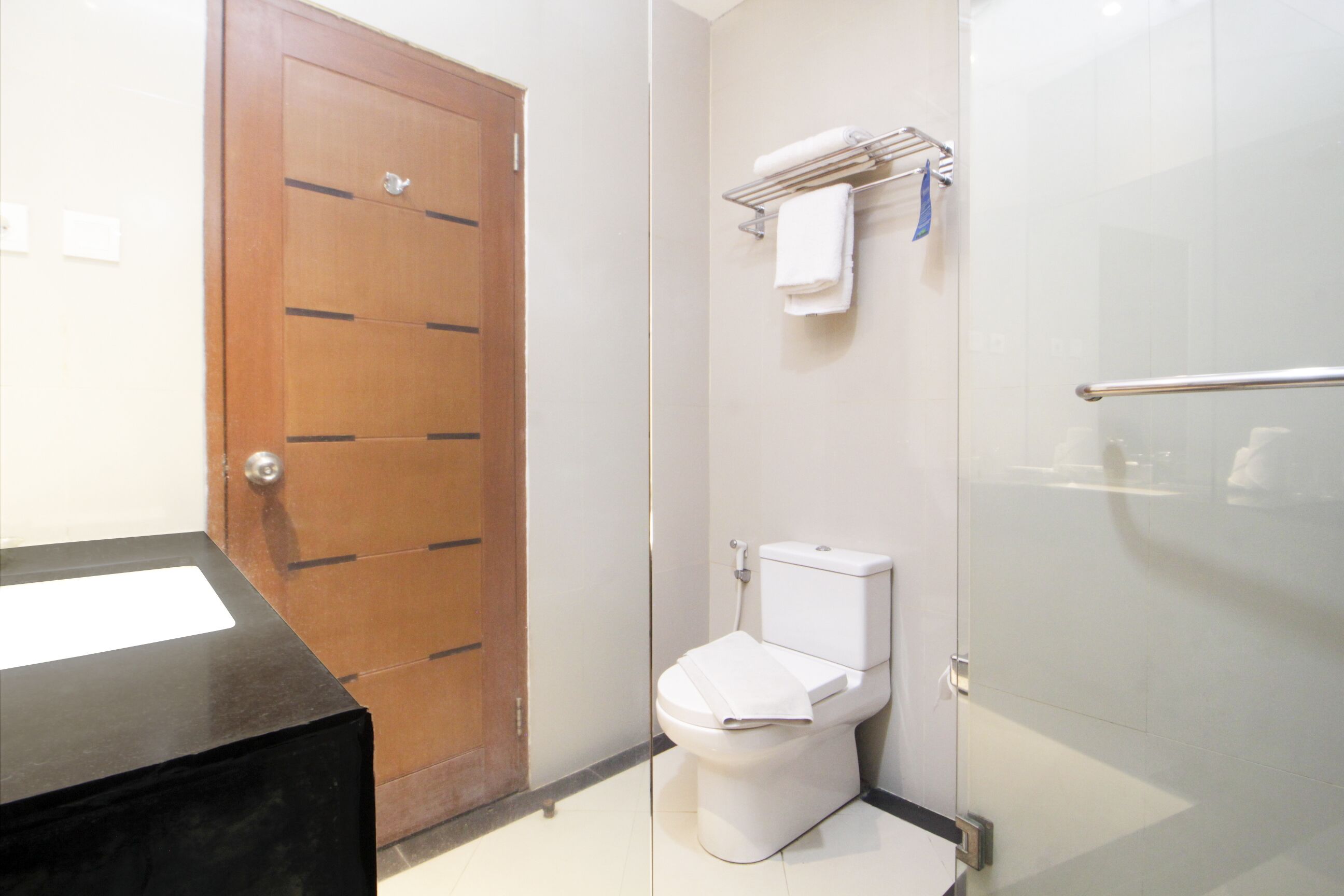 A bathroom with a wooden door, a white toilet, a glass shower enclosure, and a towel rack with a towel.