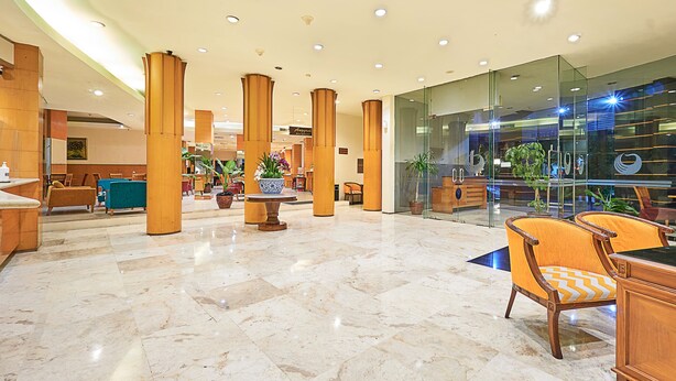 A spacious lobby with marble flooring, wooden pillars, and modern seating areas.