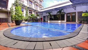 A swimming pool with a tiled edge, surrounded by a covered walkway and a building with multiple windows and a fitness room sign.