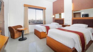 A hotel room with two beds, a small table, a chair, a window with curtains, and a city view.
