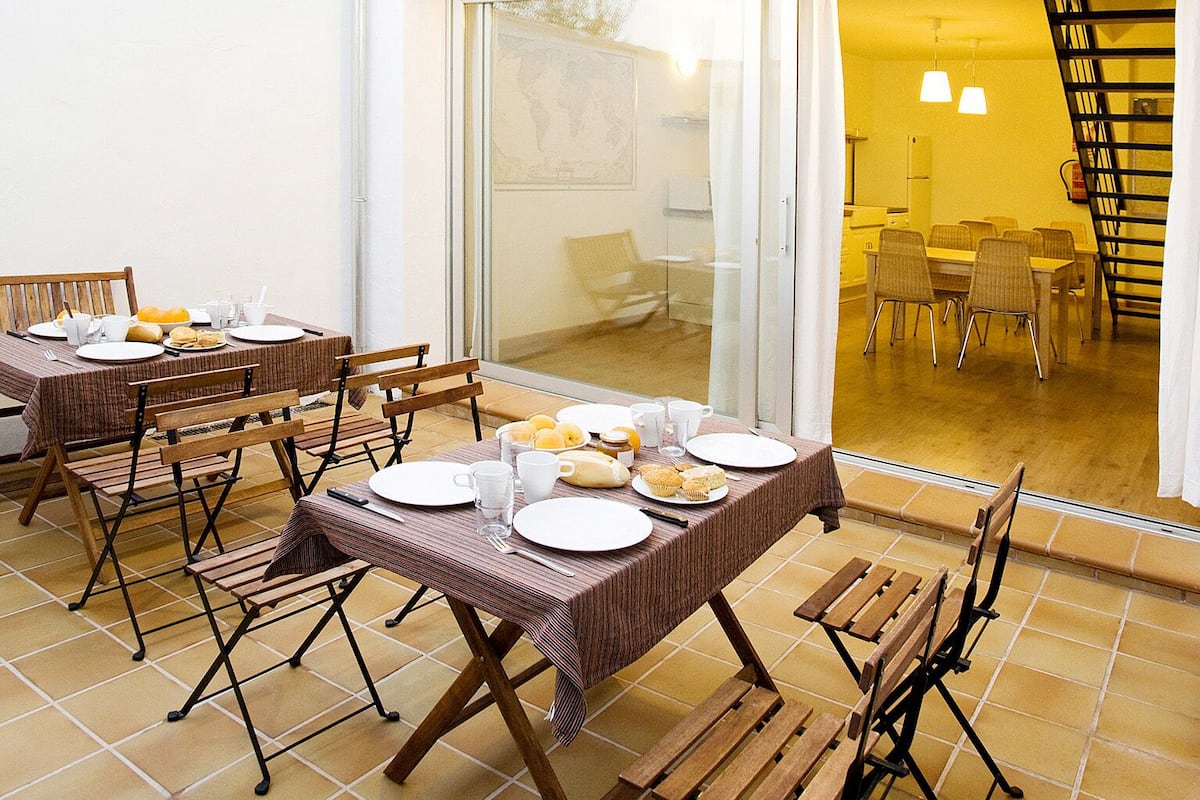 Un espace extérieur aménagé pour les repas, avec une table dressée pour quatre personnes, entourée de chaises en bois.