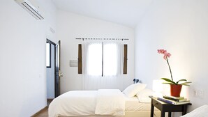 A bedroom with a bed, a bedside table with books, a potted plant, and a window with curtains. - Casa Babel Monfragüe (Torrejon El Rubio)