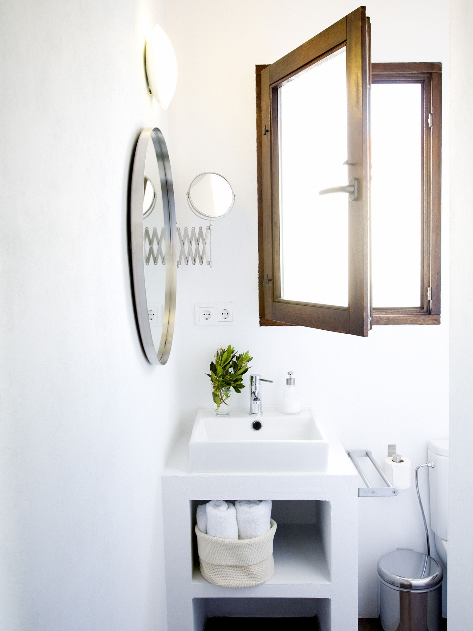Een badkamer met een witte wasbak, een spiegel, een raam en een handdoekhouder.