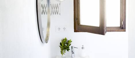 Een badkamer met een witte wasbak, een spiegel, een raam en een handdoekhouder.