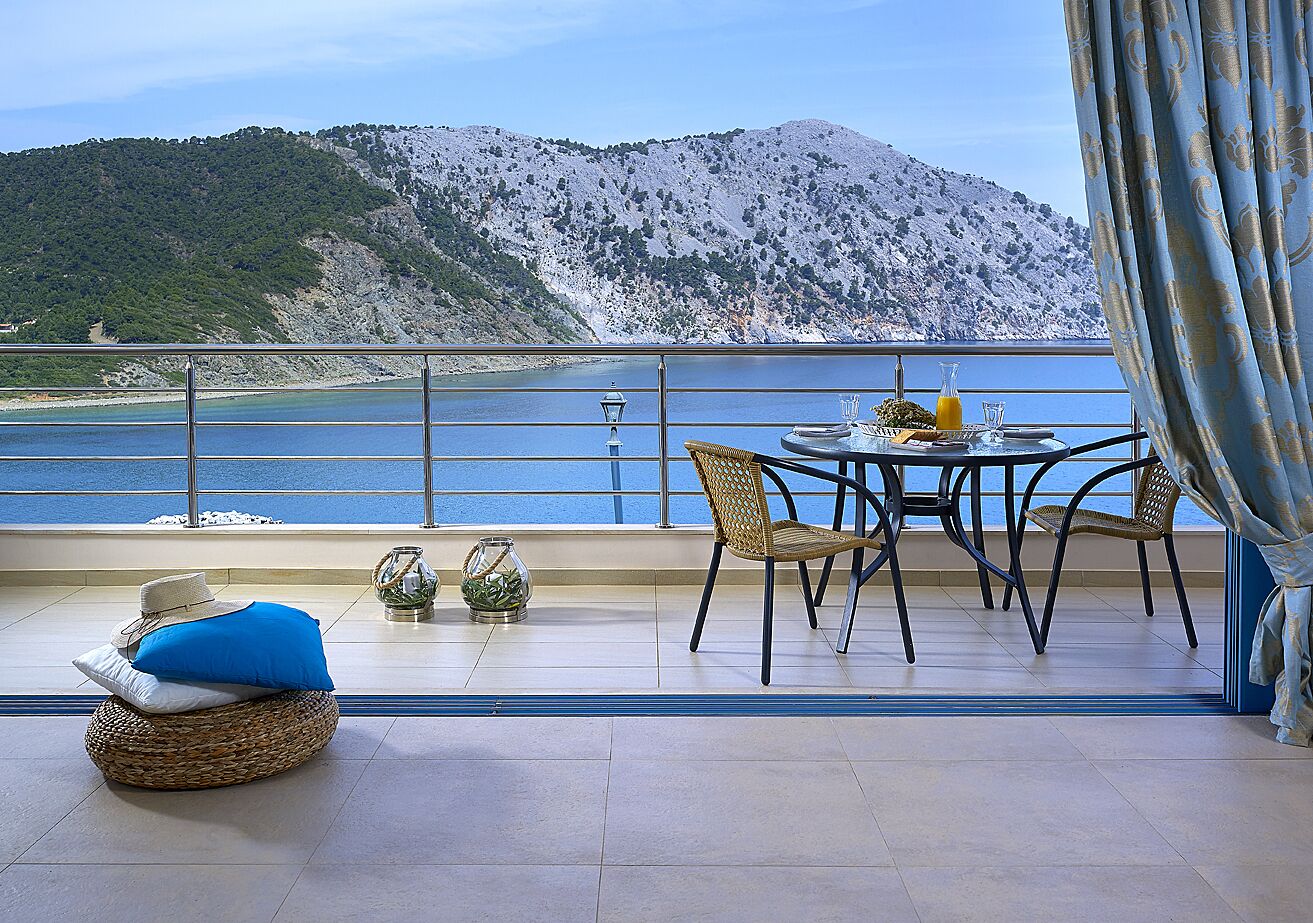 Una terraza con mesa y sillas, con vista a un cuerpo de agua y montañas.