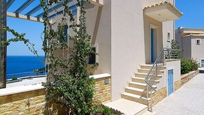 Un edificio moderno con una escalera que lleva a una puerta, vista al mar y un muro de piedra.