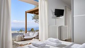 Habitación de hotel con cama, televisión, vista al mar, una silla de mimbre y una mesita.