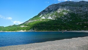 Paisaje costero con montaña rocosa, cielo azul claro y mar tranquilo.