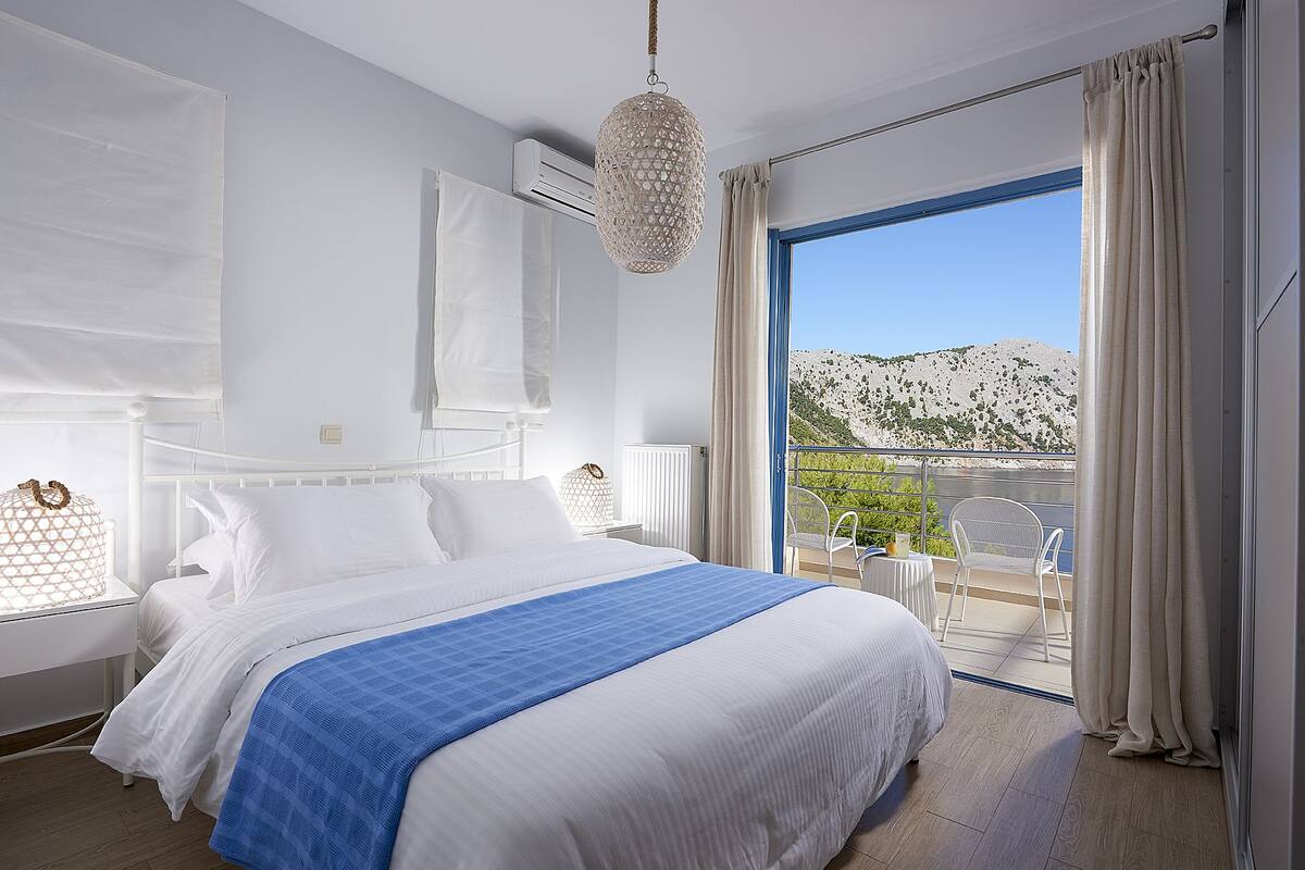 A bedroom with a large bed, a balcony with a view of a mountainous landscape, and a hanging light fixture.