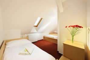 A hotel room with a bed, a desk, a radiator, a window, and a vase with flowers. - Penzion Krumlov - Massage studio (Cesky Krumlov)