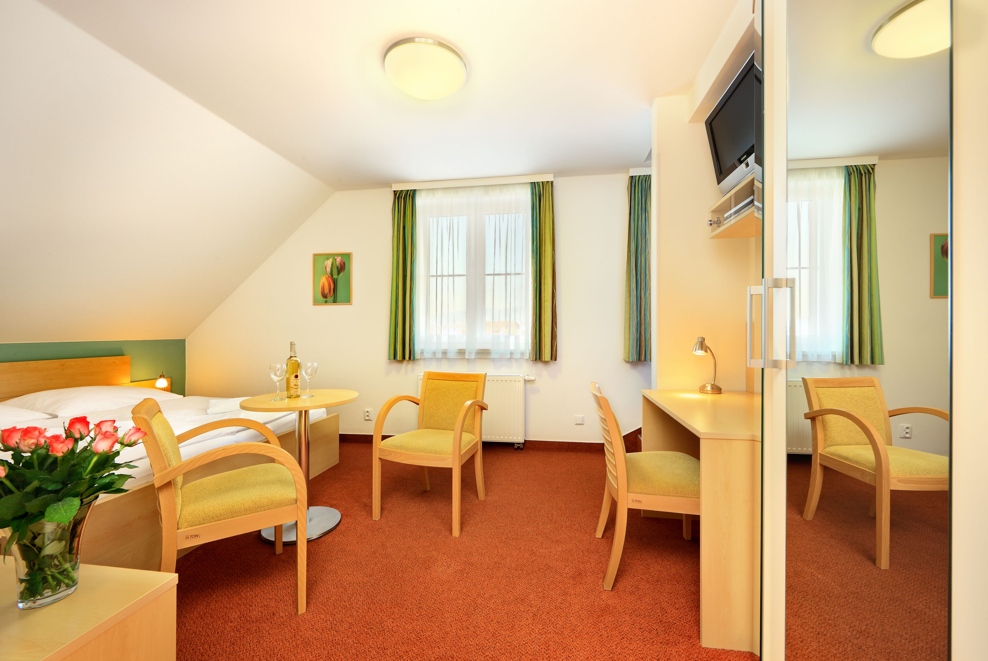 Habitación de hotel con cama, dos sillas, una mesita, televisor y ventana con cortinas.