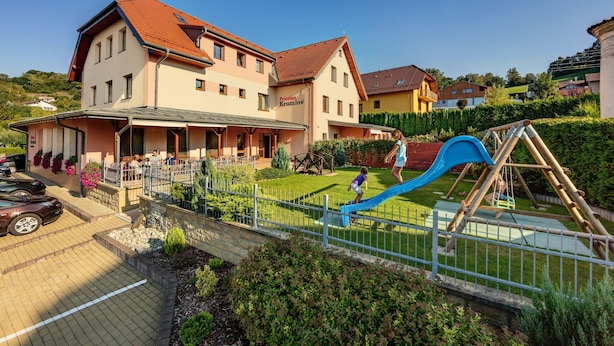 Ein Gebäude mit rotem Dach, ein Spielplatz mit blauer Rutsche und ein Parkplatz mit Autos.