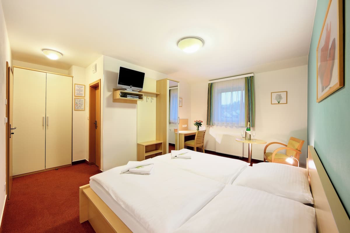 Une chambre d’hôtel avec un lit, un bureau, une chaise, une télévision et une fenêtre avec des rideaux.