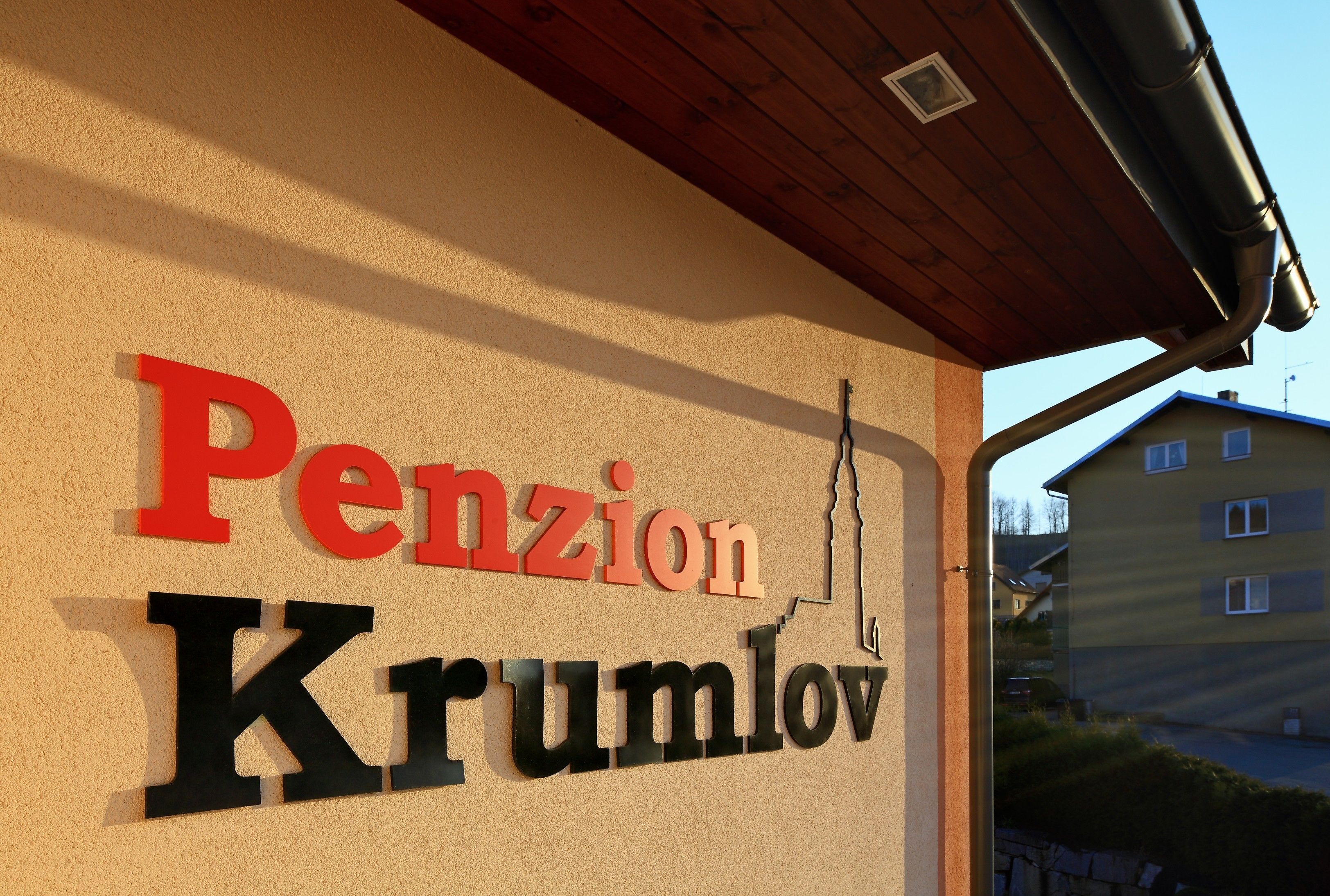 Una señal con el texto 'Pension Krumlov' sobre una pared color beige.