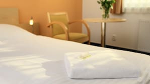 Ein ordentlich bezogenes Bett mit einem gefalteten weißen Handtuch in einem Hotelzimmer.