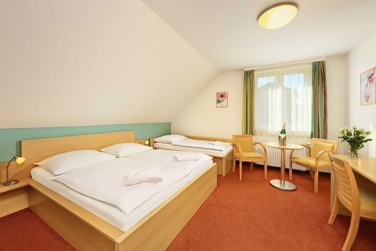 Une chambre d’hôtel avec deux lits, un bureau, une chaise, une petite table et une fenêtre avec des rideaux.