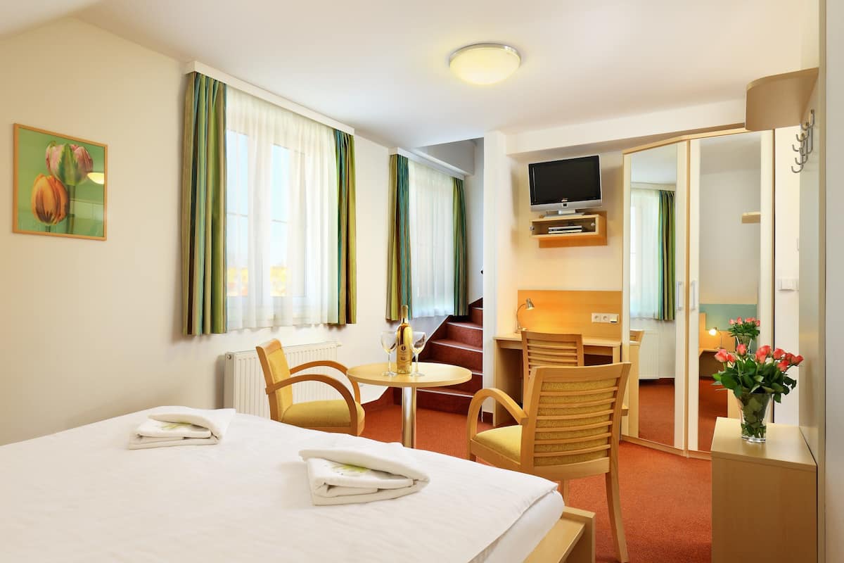 Une chambre d’hôtel avec un lit, deux chaises, une petite table avec une bouteille, un téléviseur et un miroir.
