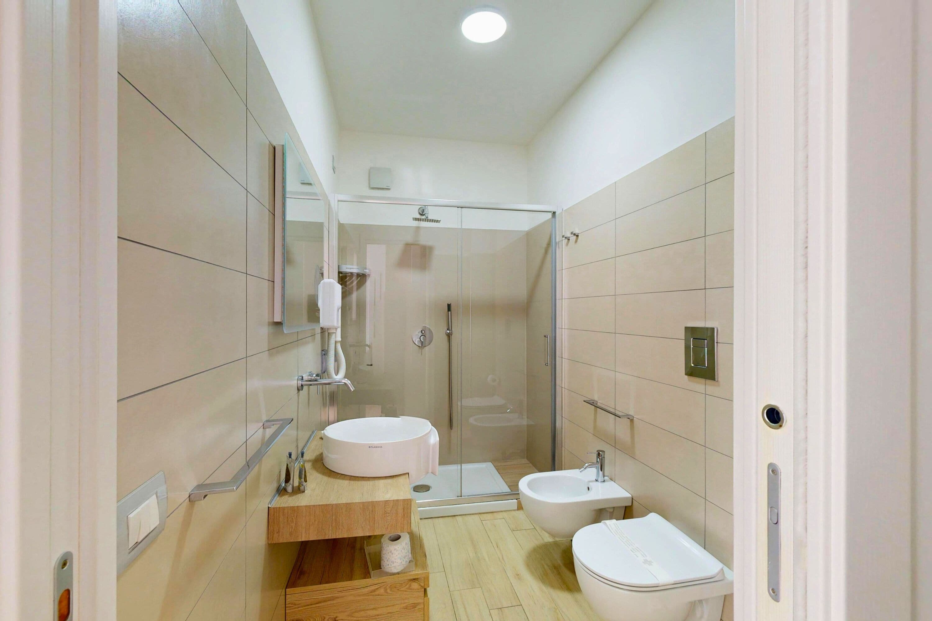 Une salle de bain moderne dotée d’une douche à parois de verre, d’un meuble-lavabo en bois, d’un lavabo blanc et d’un bidet.