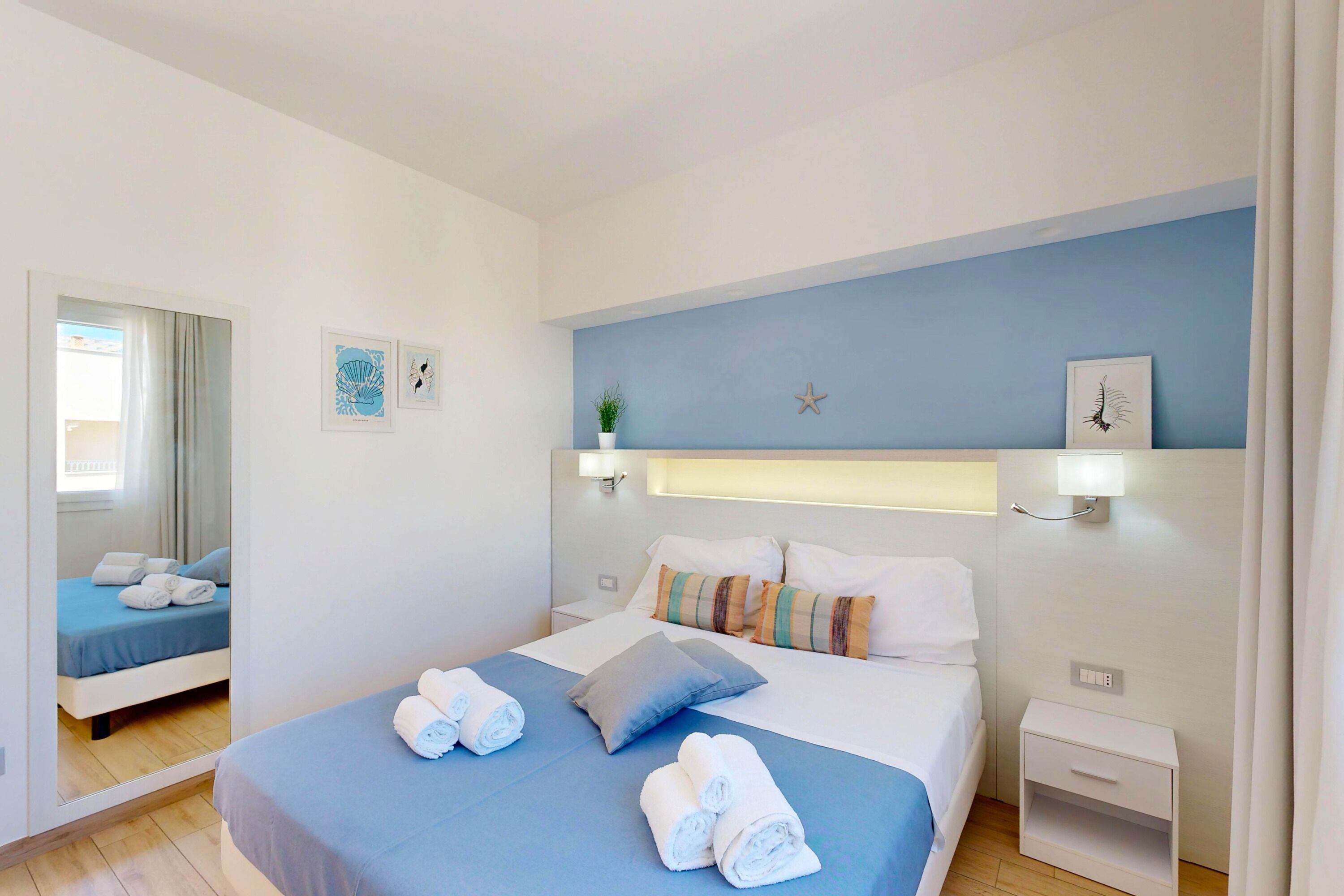 Una habitación de hotel con una cama, mesitas de noche, un espejo y luces fijadas a la pared.